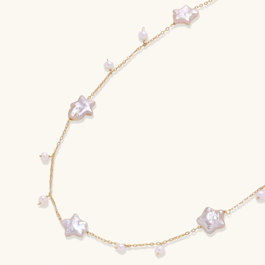 Gold vermeil chain with iridescent star-shaped baroque pearls and small round freshwater pearl drops on cream background.