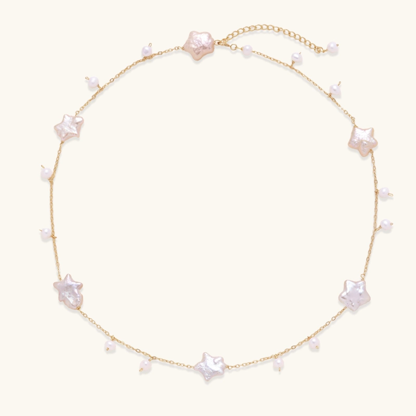 Gold vermeil chain with iridescent star-shaped baroque pearls and small round freshwater pearl drops on cream background.
