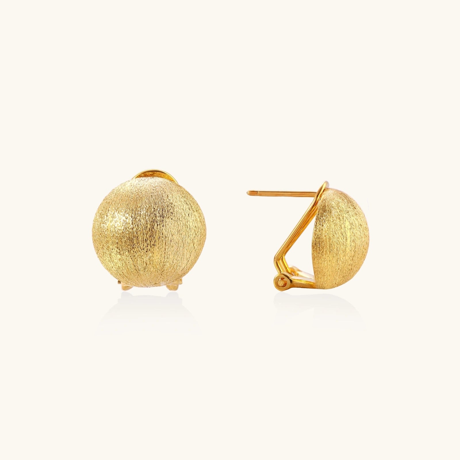Pair of brushed gold dome earrings with clip backs showing textured matte finish on cream background